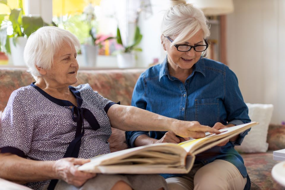 一位老年妇女和一位中年妇女坐在沙发上看相册。