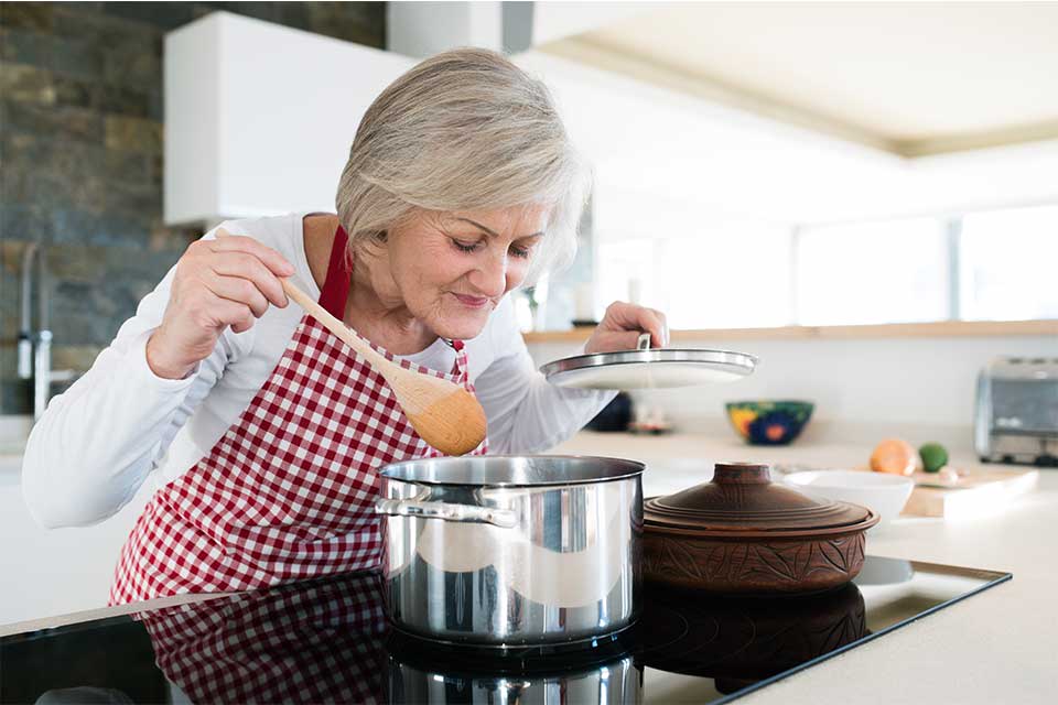 老妇人烹饪意大利面酱在她的炉灶。
