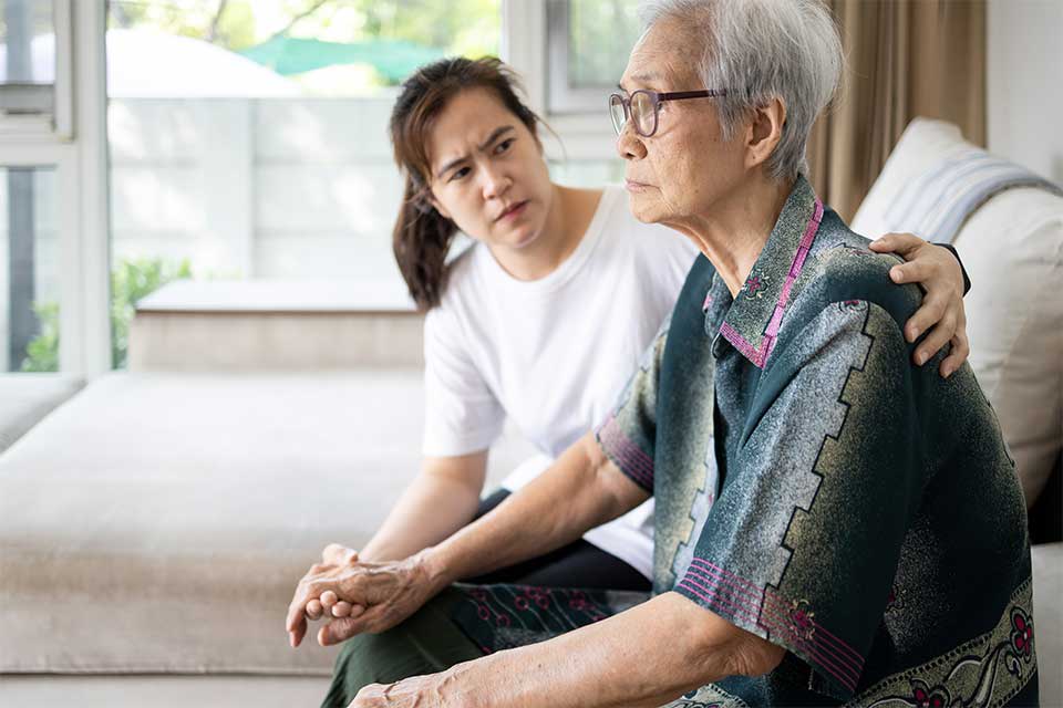 一位老妇人和她的看护人坐在沙发上，试图提供情感支持。
