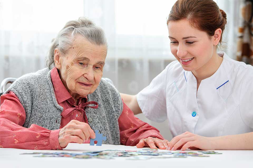 一位老年妇女在看护者的帮助下拼拼图
